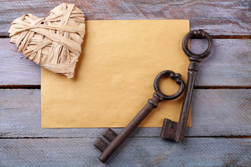 Old key with decorative heart and sheet of paper on blue wooden background, close up