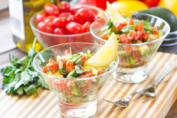 Sauce guacamole o salad in glass bowls and ingredients - avocado, tomatoes, lemon, cilantro and olive oil. Latinamerican food