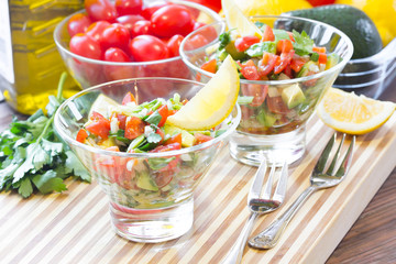 Sauce guacamole o salad in glass bowls and ingredients - avocado, tomatoes, lemon, cilantro and olive oil. Latinamerican food