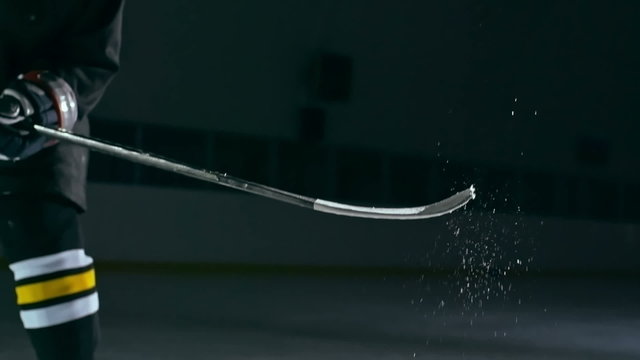 Slow motion shot of hockey player tossing up a puck with his stick at dark ice arena 