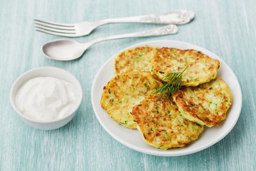 Vegetable zucchini cabbage pancakes or fritters with sour cream on wooden kitchen table