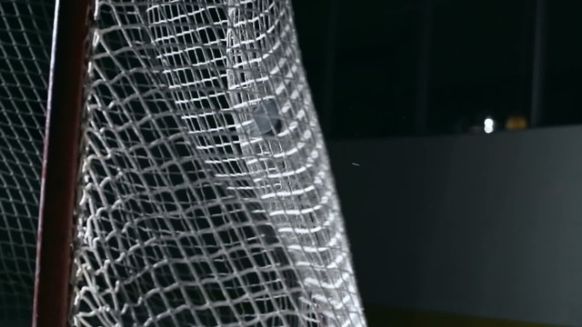 Slow motion shot of hockey puck flying into net of ice hockey goal at dark arena