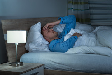 Man Suffering From Headache Lying On Bed