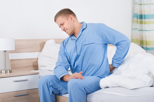 Man With Back Pain Sitting On Bed