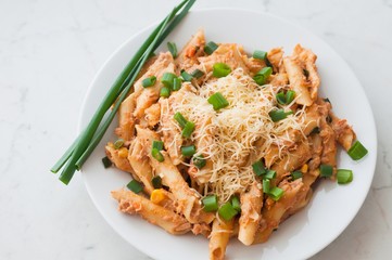 Penne pasta with healthy tuna fish, cheese and chopped scallion or spring onion leaves. Served on a white oval plate
