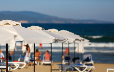 White beach umbrellas on a blurred background of blue sea and the mountains. White parasols. Blurred beach background. Shallow depth of field. Selective focus.