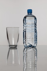 plastic bottle with water and empty glass next to bottle