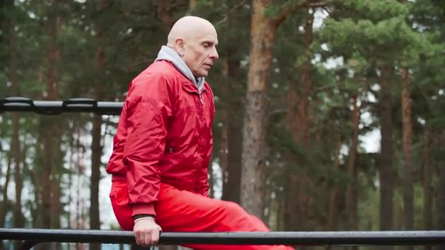 Mature sportsman holding l-sits on parallel bars outdoor