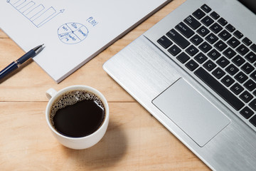 laptop and coffee cup with business plan on wooden table
