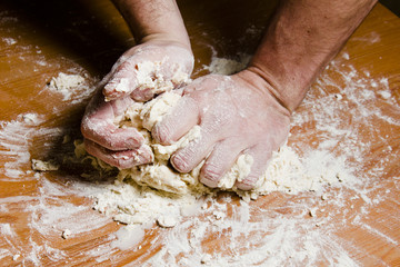 Men's hands knead the dough on the wooden table. The chef prepares the dough for Italian cuisine.