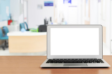 blank screen laptop on wooden table with blur hospital background