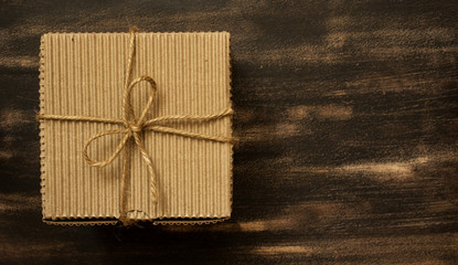 Cardboard gift box with bowknot made of rope on a brown wooden background