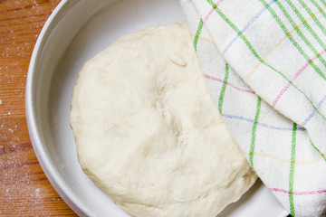 The dough in the bowl under a towel. Preparations for baking the dough in a rustic style.