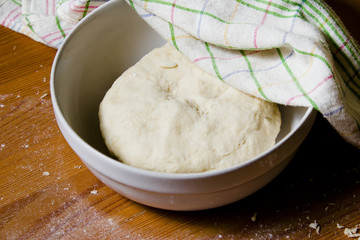The dough in the bowl under a towel. Preparations for baking the dough in a rustic style.