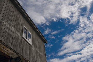 The old building with a window. Bright blue sky with clouds on a sunny day. reflection of clouds in building windows. The dilapidated natural wood board.

