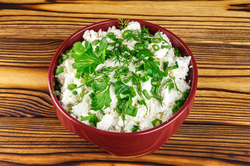 Fresh cottage cheese with sour cream, dill, parsley, onion in ceramic bowl on wooden table