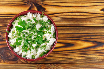 Fresh cottage cheese with sour cream, dill, parsley, onion in ceramic bowl on wooden table, top view