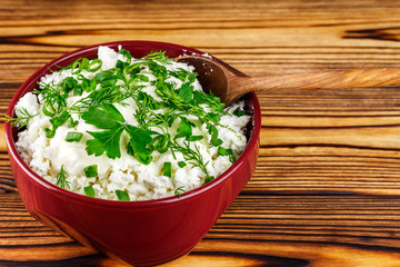 Fresh cottage cheese with sour cream, dill, parsley, onion and spoon in ceramic bowl on wooden table, space for text