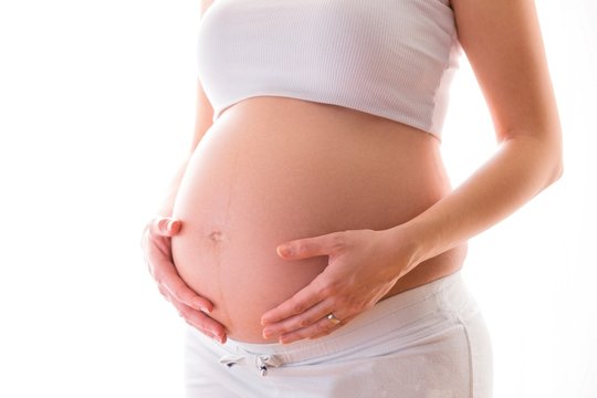Close up of a pregnant woman gently touching her belly.