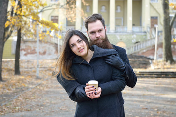 Fashion portrait of young couple drinking coffee in autumn park