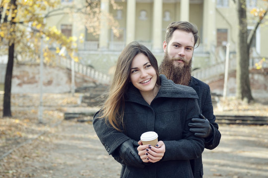 Fashion portrait of young couple drinking coffee in autumn park