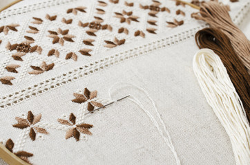 The wooden hoop with the embroidery pattern of brown and beige color on canvas, on wooden table.Rustic style. Selective focus.