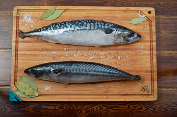 Two mackerels on wooden plate with spices from top