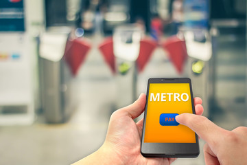 hand hold smartphone and finger touch on pay button for metro fare payment with blur metro gate background