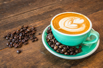 Latte hot coffee in green cup with latte art and roasted coffee beans. Wooden table background. In coffee shop.