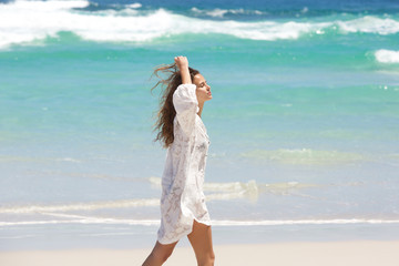 Young woman walking on beach with hand in hair