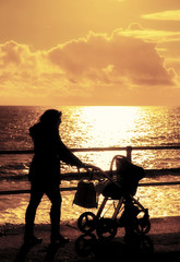 Mum with pram walking along sea front silhouettte