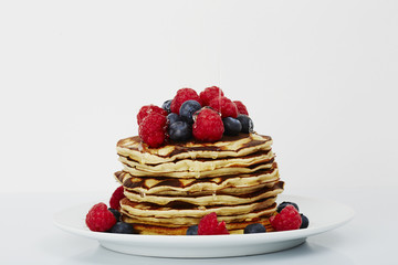 Pancakes topped with fruit and honey in white studio