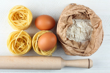 the rolling pin and pasta with eggs and flour in bag on white wooden table