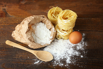 pasta with eggs and sprinkled with flour with wooden spoon on brown wooden table