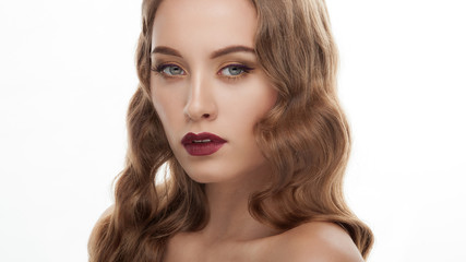 Fototapeta premium Closeup portrait of young elegant blonde woman with wavy hairstyle gorgeous fashionable makeup posing with half closed eyes and bare shoulders on white studio background