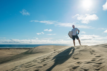 Young man posing with board at Te Paki sand dunes, New Zealand