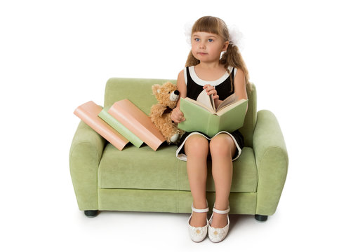 Pretty Little Blonde Girl With Groomed Long Hair And Short Bangs,reading A Book Sitting On A Green Couch - Isolated On White Background