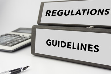Fototapeta premium Regulations and Guidelines - two binders on white background with calculator and pen