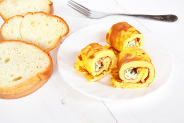 Rolls of omelette with cheese on a plate on white wooden background, bread, fork