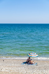 Fototapeta na wymiar Couple in swimsuits sitting on beach under umbrella and watching the sea in Novyi Svit, Crimea, Ukraine