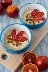 Tasty oatmeal with sicilian orange slices and raisins on blue bowls on wooden background