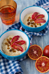 Tasty oatmeal with sicilian orange slices and raisins on blue bowls on wooden background