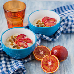 Tasty oatmeal with sicilian orange slices and raisins on blue bowls on wooden background