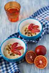Tasty oatmeal with sicilian orange slices and raisins on blue bowls on wooden background