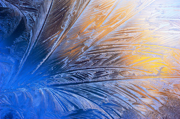 Window glass covered with ice pattern against sunset