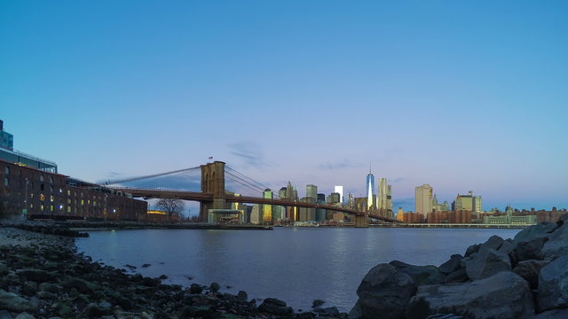 USA. New York. Dawn over Manhattan, Brooklyn bridge and the rocky shore of the East River at Main Street Park. Time lapse