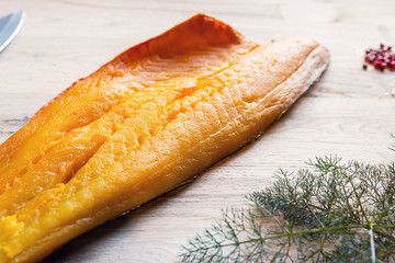 beautiful yellow smoked haddock fish fillet with a branch of fresh dill weed, salt and pink berry on a natural oak tree table