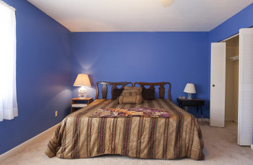 Dated simple bedroom with blue walls and popcorn ceiling