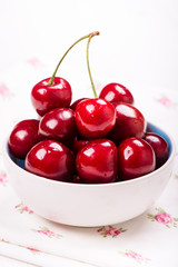 Closeup of red cherries with water drops in white bowl on napkin with roses on table