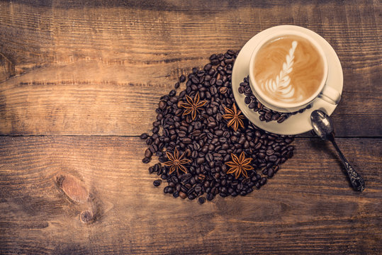 a cup of cappuccino  with cinnamone and star anise on vintage wooden background